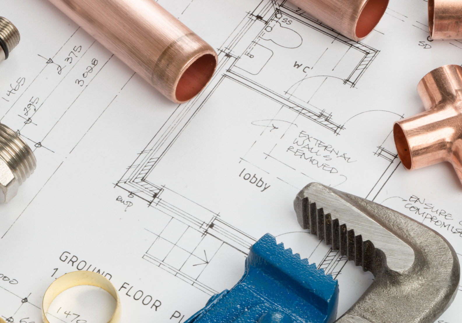 Various plumbers tools and plumbing materials including copper pipe, elbow joint, wrench and spanner. shot on top of architects house plans on a bright stainless steel background.